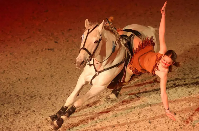 Une fille reste en équilibre sur le côté d'un cheval au galop